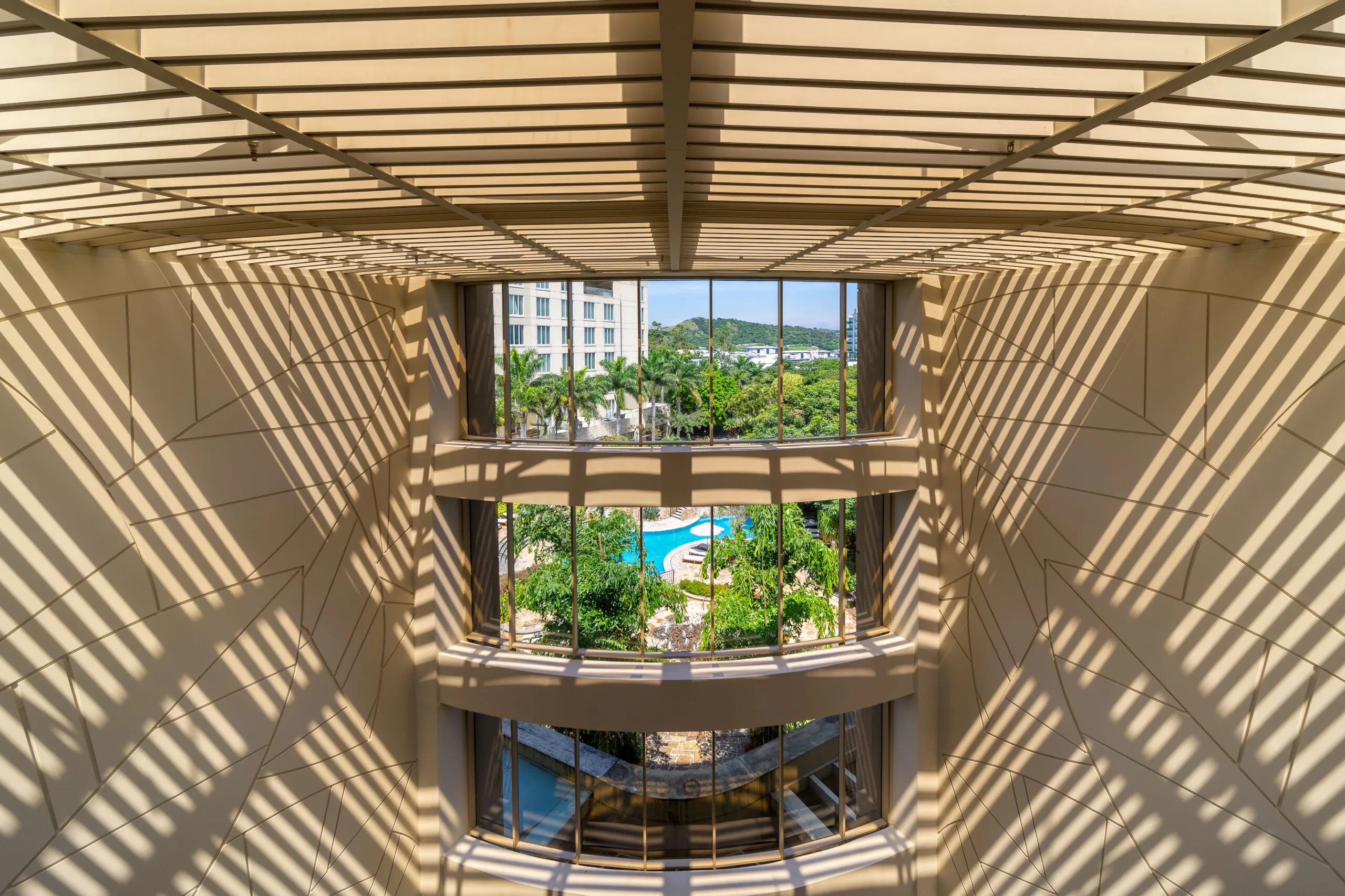 Vista interior con sombras de lamas sobre un jardín y piscina