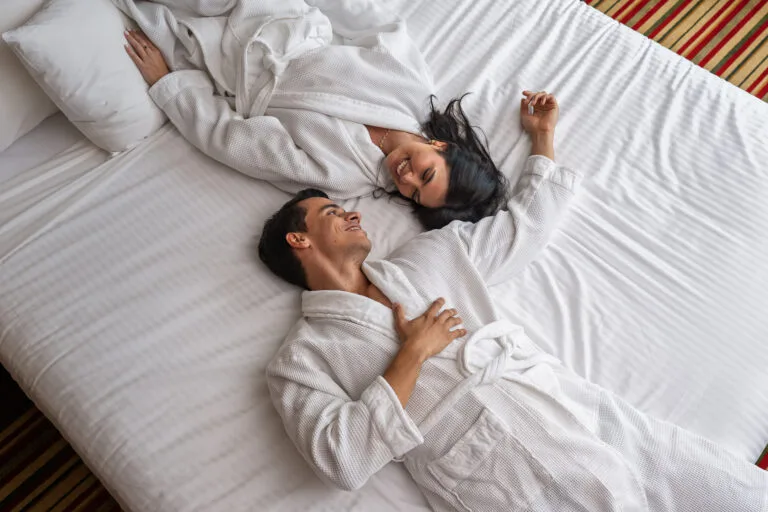 Pareja relajada en una cama de hotel, usando batas de baño.