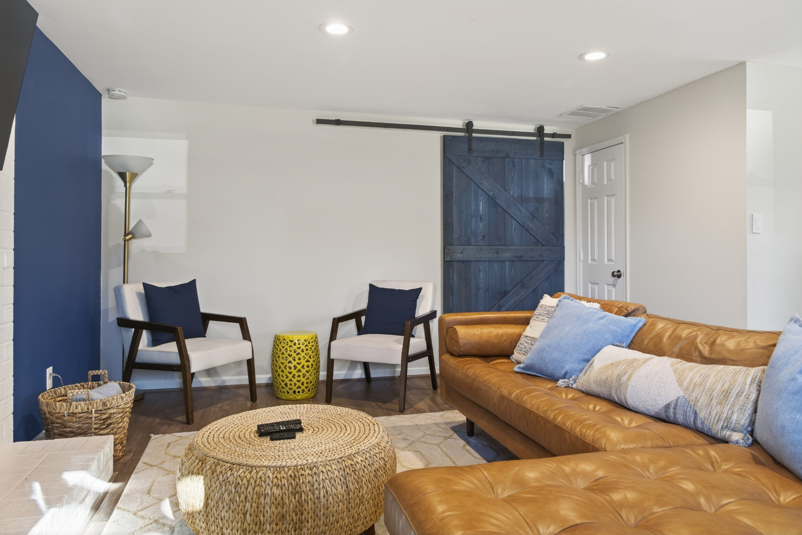 Sala moderna con sofá de cuero, sillas blancas y puerta corrediza de madera.
