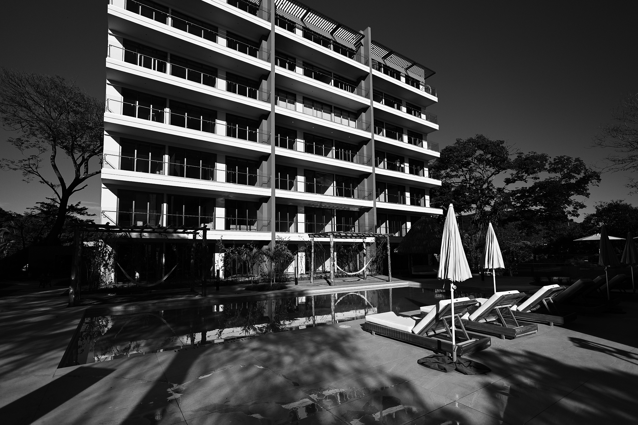 Fachada de hotel moderno con piscina y camastros.