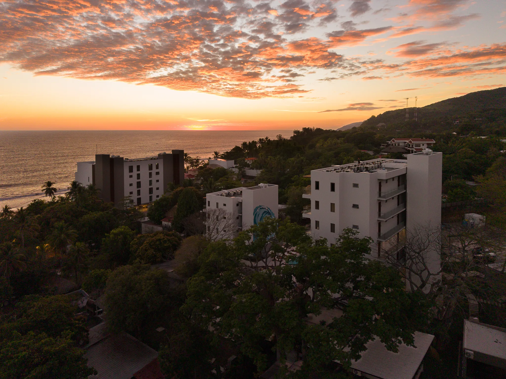 Vista aérea al atardecer de los edificios residenciales de Zonset entre vegetación, con el océano de fondo en Playa El Zonte, El Salvador.